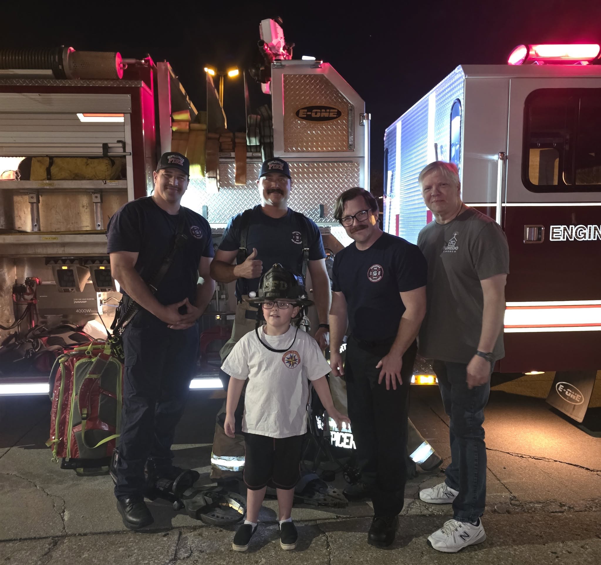 Tim Sherrick with Fire Station 3 firefighters and a child in a fire helmet in front of a fire engine
